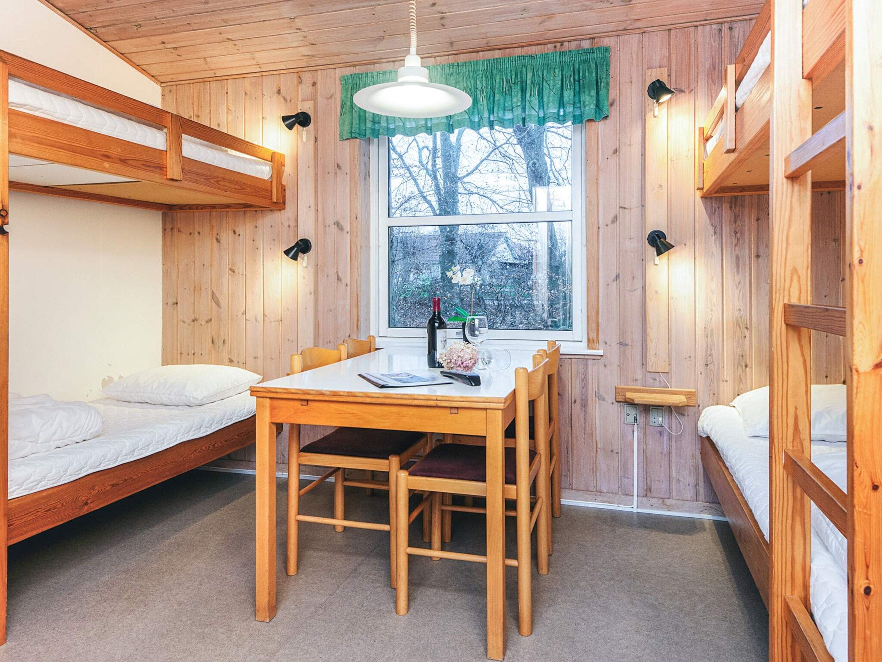 A cabin with bunk beds, a dining table, and a window with a view of trees.
