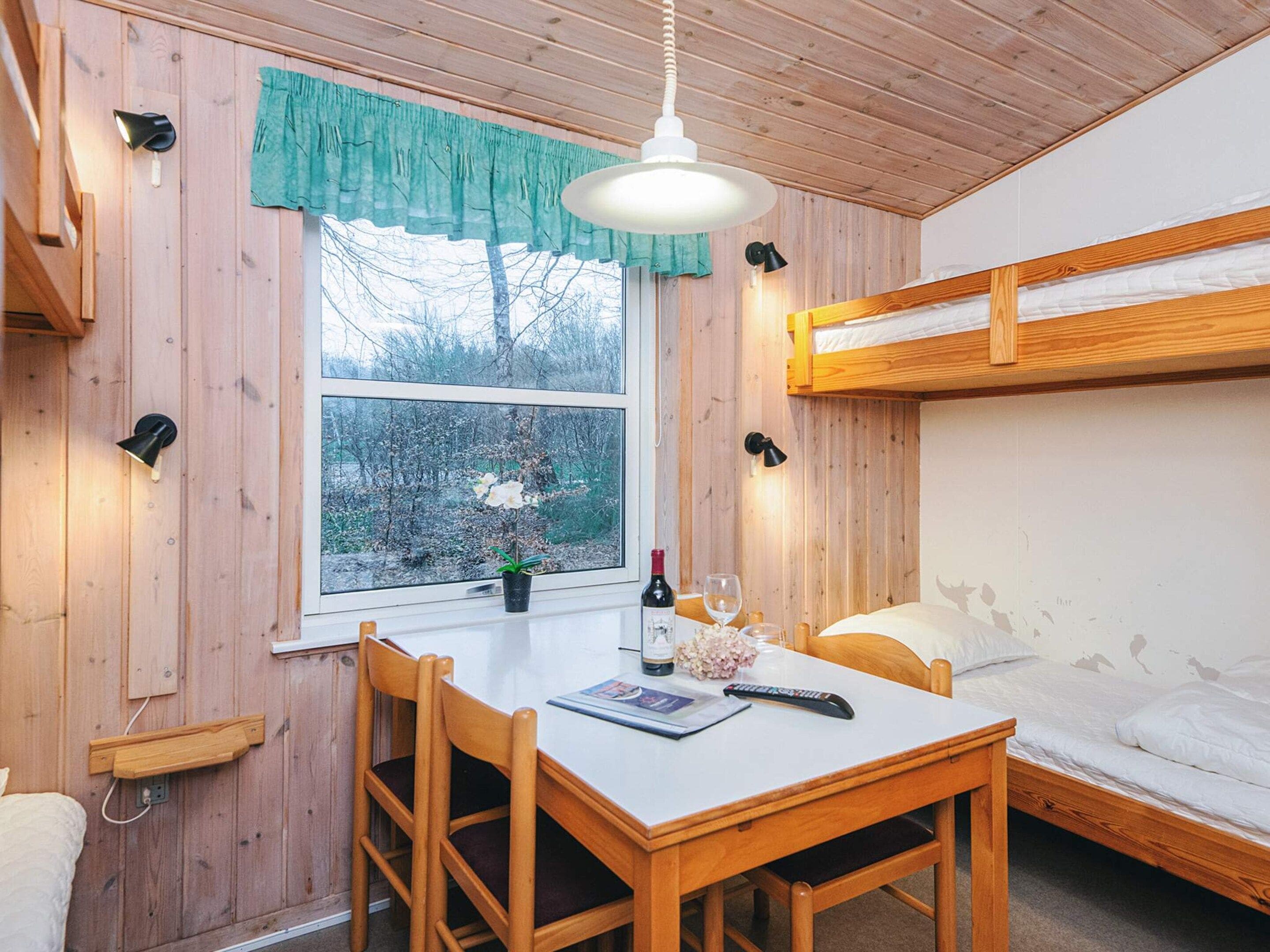 Une petite pièce avec un lit superposé, une table avec une télécommande, une bouteille et un verre.