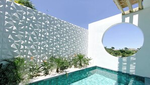 Un espace piscine moderne avec des murs aux motifs géométriques, une piscine à l’eau d’un bleu limpide et une fenêtre circulaire offrant une vue sur les environs.