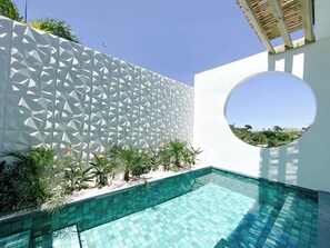 Ein moderner Poolbereich mit geometrisch gemusterten Wänden, einem klaren blauen Pool und einem runden Fenster, das einen Blick ins Umland ermöglicht.