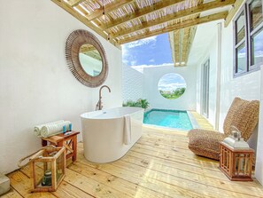 Ein modernes Badezimmer mit einer freistehenden Badewanne, einem runden Spiegel und Blick auf einen Swimmingpool.