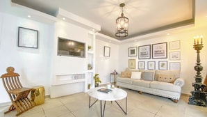 Un salon comprenant un canapé, une table basse, un téléviseur fixé au mur et un lustre.