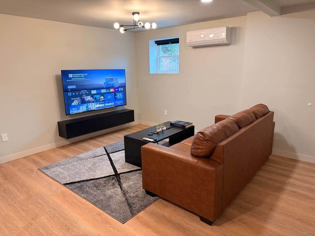Una sala de estar moderna con un sofá de cuero marrón, una mesa de centro negra y un televisor de pantalla plana montado en la pared.