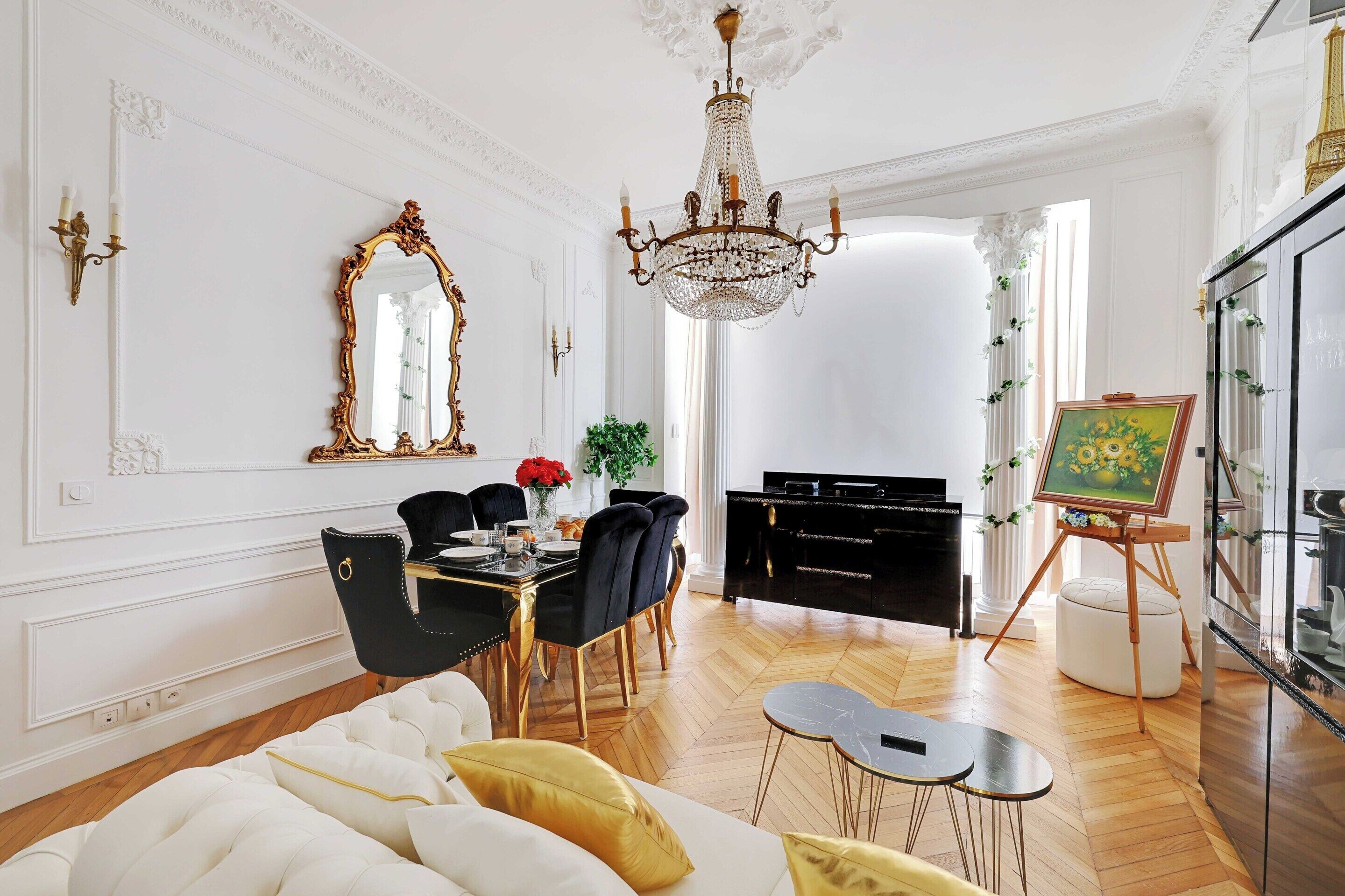A dining area with a black table, white upholstered chairs, and a chandelier.