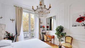 Et soveværelse med en stor seng, en lysekrone, en stol, et bord og en potteplante.