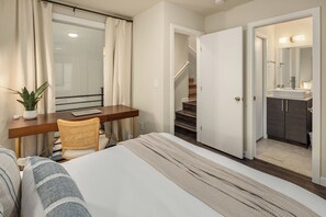 Une chambre d’hôtel avec un lit, un bureau, une chaise, une plante en pot et une vue sur une salle de bain équipée d’un lavabo et d’un miroir.