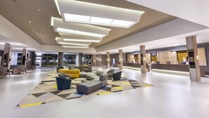 A spacious lobby with a modern design, featuring a large seating area with sofas and armchairs, a reception desk, and a geometric patterned carpet. - Riu Chiclana (Chiclana de la Frontera)
