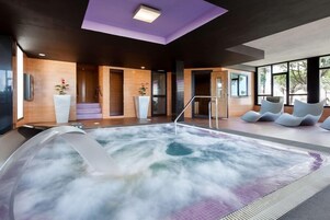 A modern spa area with a hot tub, wooden walls, and a view of trees.