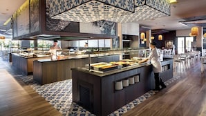 A modern buffet area with multiple serving stations, a central island with a server, and patterned ceiling designs. - Riu Chiclana (Chiclana de la Frontera)