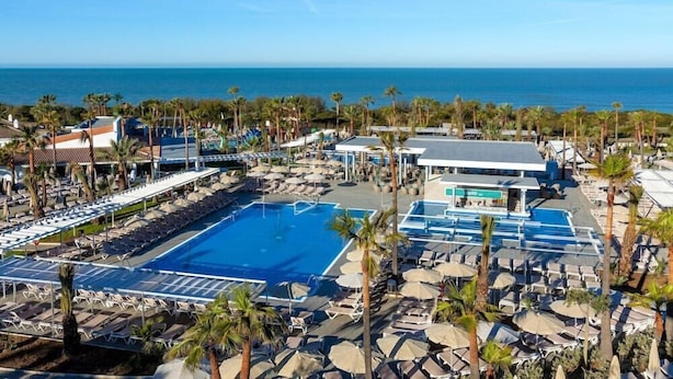 A resort with a large swimming pool, multiple lounge areas, and a view of the ocean. - Riu Chiclana (Chiclana de la Frontera)
