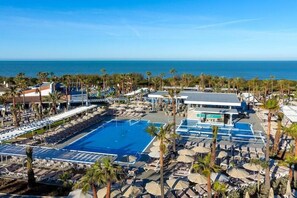 Un complejo turístico con una gran piscina, varias zonas de descanso y vistas al océano.