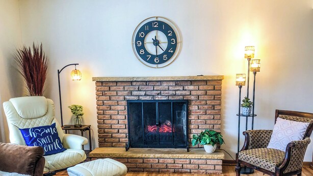 Una sala de estar con chimenea de ladrillo, un reloj de pared redondo y dos lámparas de pie.