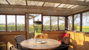 Una habitación soleada con una mesa redonda de madera, sillas y ventanas amplias que dan a un campo verde.