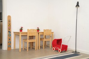 Ein Zimmer mit Holztisch und -stühlen, einem roten Spielzeugauto, einer Stehlampe und einer Holz-Wachstumsleiste.