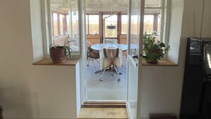 Vista a través de un ventanal a un cuarto con una mesa redonda, sillas y plantas en macetas.