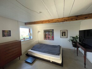 Une chambre à coucher avec un lit, une commode, une fenêtre, des tableaux et un téléviseur.