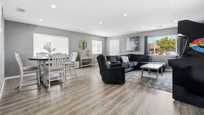 Un salon spacieux comprenant un coin repas, un canapé noir et un fauteuil noir.