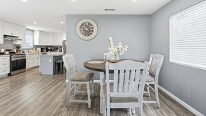 Une cuisine moderne avec des meubles blancs, une table de salle à manger ronde entourée de chaises blanches et une horloge au mur.