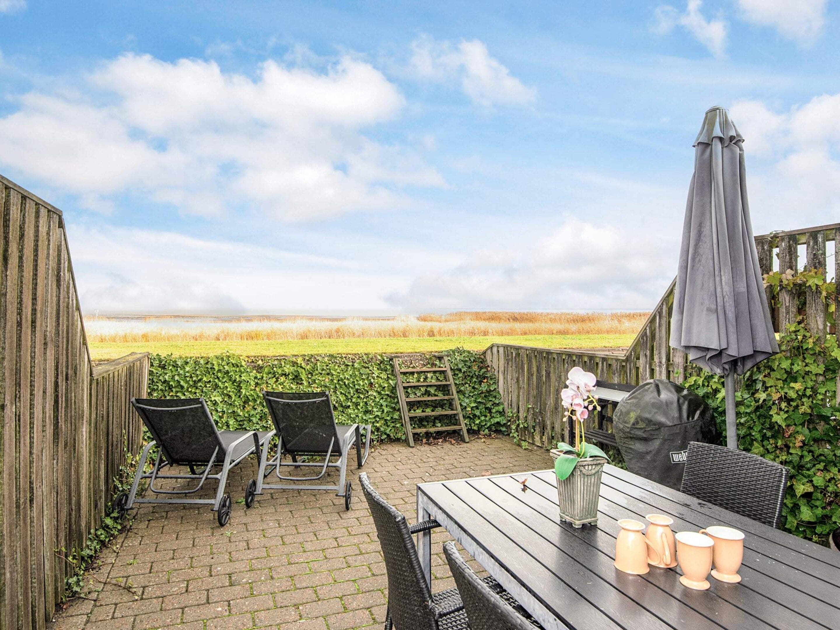 A patio with a view of a field, a table with chairs, and a covered area.