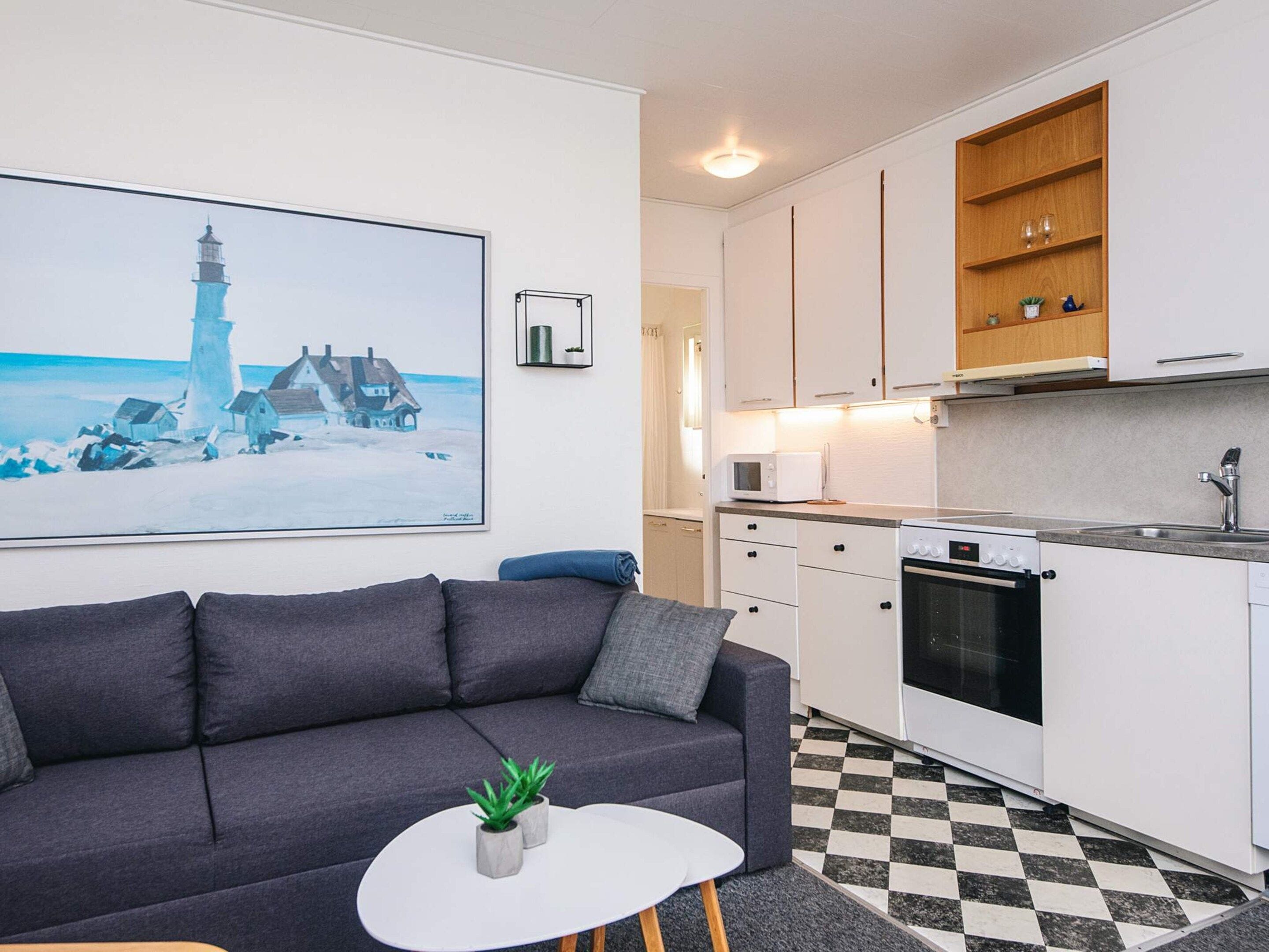 A modern living room with a grey sofa, a white coffee table, and a painting of a lighthouse.