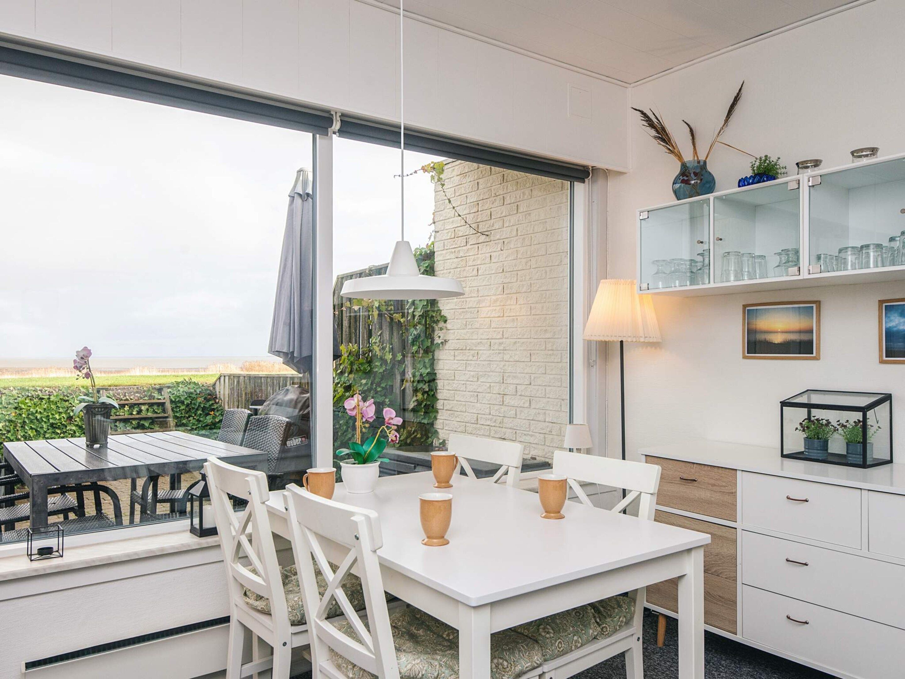 A dining area with a white table and chairs, a hanging light fixture, and a view of the outdoors.