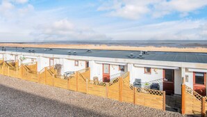 A row of white buildings with numbered doors, a gravel path, and a view of the beach. - 4 Person Holiday Home in Romo (Rømø)