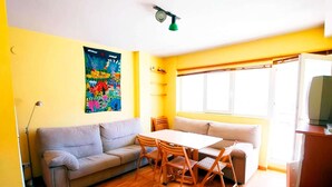 Ein Zimmer mit einer Couch, einem Esstisch mit Stühlen, einem Fenster und einem Fernseher.