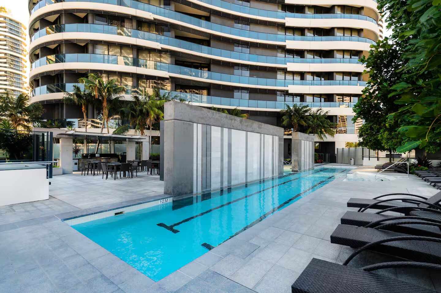 Un hôtel moderne doté d’une piscine, d’un espace extérieur aménagé et d’un immeuble à plusieurs étages en arrière-plan.