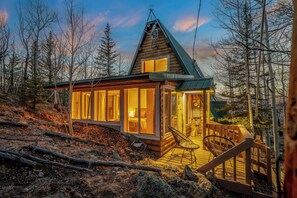 A log cabin with a wooden deck and a glass-enclosed porch. - Sunset View A Frame: Privacy, Hot Tub, Pet Friendly, Mid-Mod Vibes (Jefferson)