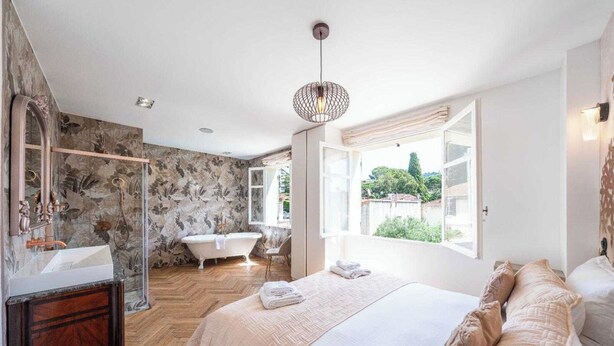 Una camera da letto con un letto grande, un bagno con vasca e vista su spazi verdi.