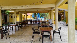 Ein Außenbereich zum Essen mit Tischen und Stühlen, ein überdachter Gang und ein Pool im Hintergrund.