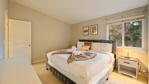 Ein Schlafzimmer mit Bett, Nachttisch, Lampe und einem Fenster mit Blick.