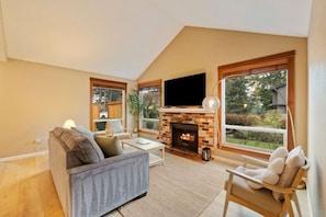 A living room with a fireplace, a sofa, a TV, and large windows. - Chic 3BR Home | Foosball • Great Location@Bellevue (Bellevue)