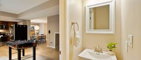 A modern kitchen with a foosball table, a dining area with chairs, and a bathroom with a sink and mirror.
