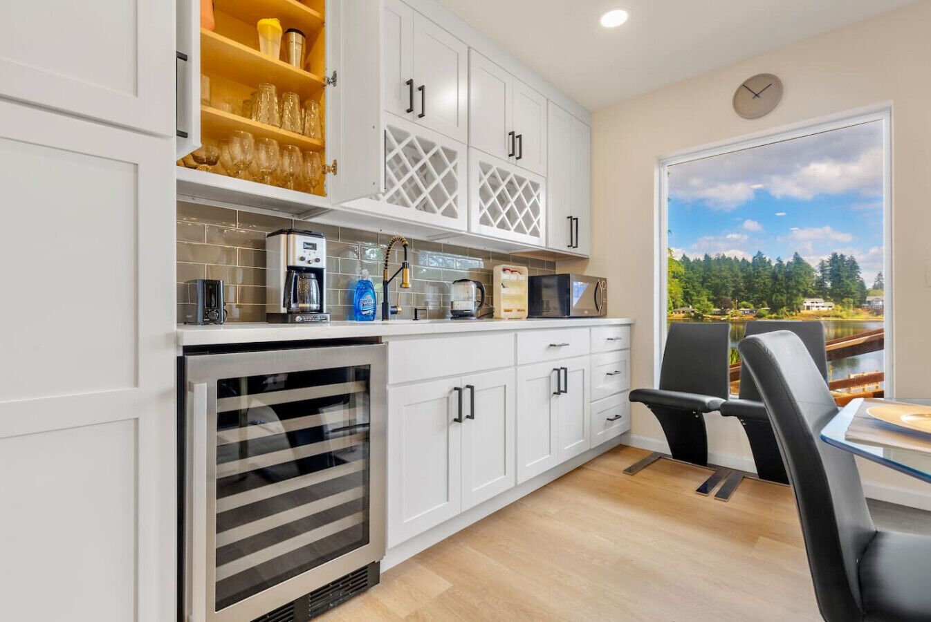 A modern kitchen with white cabinets, a built-in oven, and a dining area with a table and chairs.