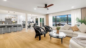 A modern living room with a sofa, two armchairs, a coffee table, and a dining area with a kitchen in the background. - Spacious 3B2B Upper unit breathtaking lake views (Auburn)