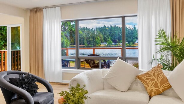 A modern living room with a large window offering a view of a lake and forest. - Spacious 3B2B Upper unit breathtaking lake views (Auburn)