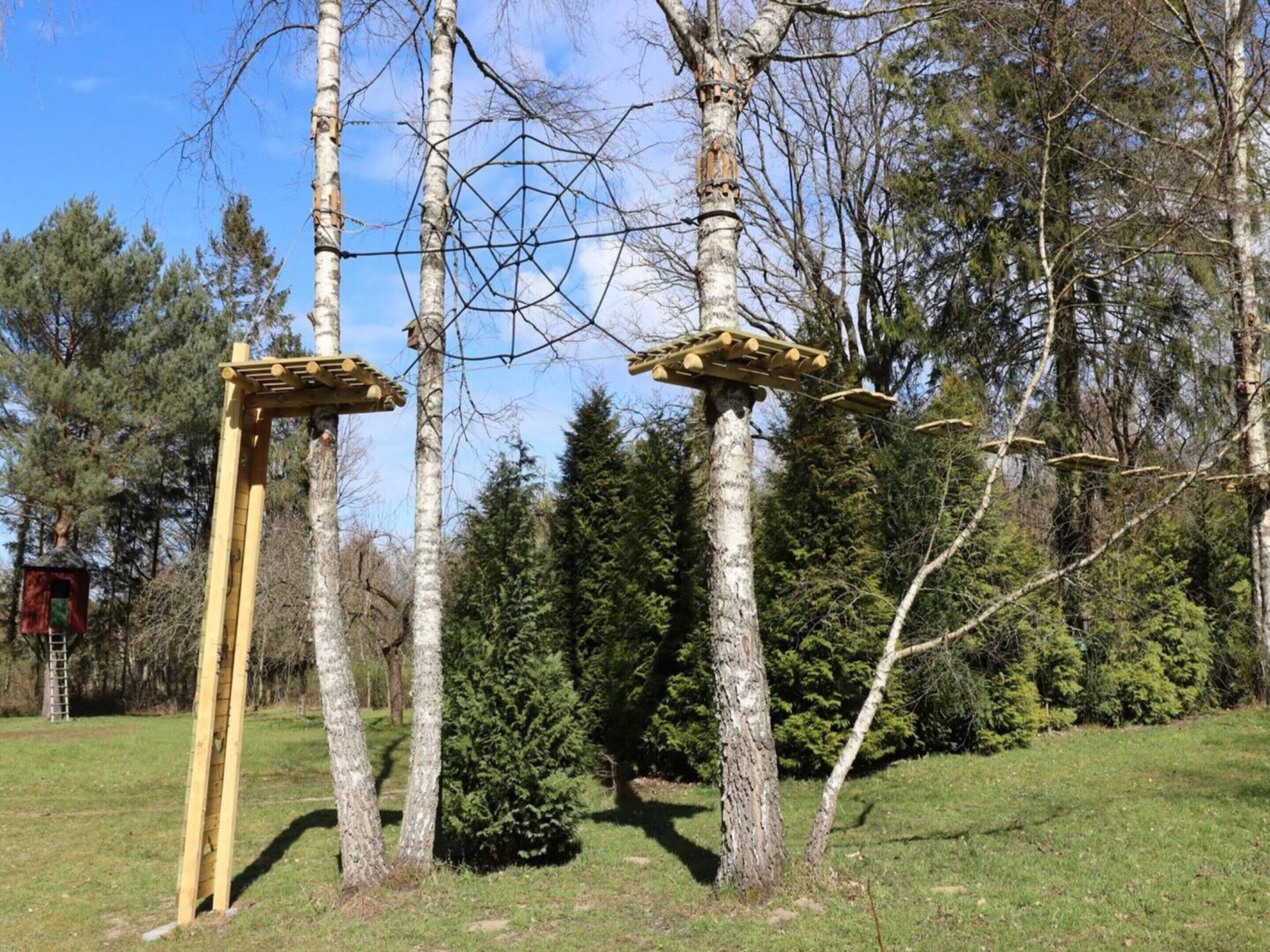 Une structure en bois, dotée d’une échelle et d’une plateforme, entourée d’arbres et d’une zone herbeuse.