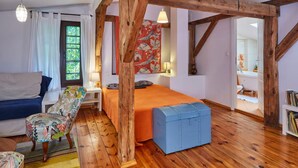 Une pièce chaleureuse avec un plafond en bois, un lit recouvert d’une couverture orange, une chaise colorée et une commode bleue.