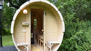 Une structure en bois comprenant un banc à l’intérieur, une porte et un petit espace de véranda.