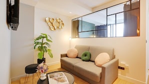 A modern living room with a sofa, a coffee table, a potted plant, and a flat-screen TV mounted on the wall. - Serene Apartment for 6p Near the Marais (Paris)