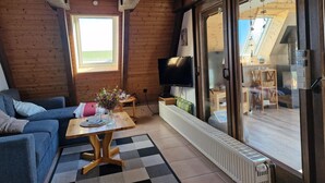 A cozy room with a sofa, a coffee table, a TV, and a large window. - Nurdachhaus in Burhave (Butjadingen)