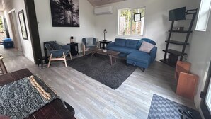 A modern living room with a blue sofa, a coffee table, and a rug. There is a painting on the wall and a window with a view of trees. - Charming Muskoka Wilderness Cottage (Windermere)