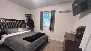 A bedroom with a bed, a wardrobe, a TV, and a window with curtains. - Charming Muskoka Wilderness Cottage (Windermere)