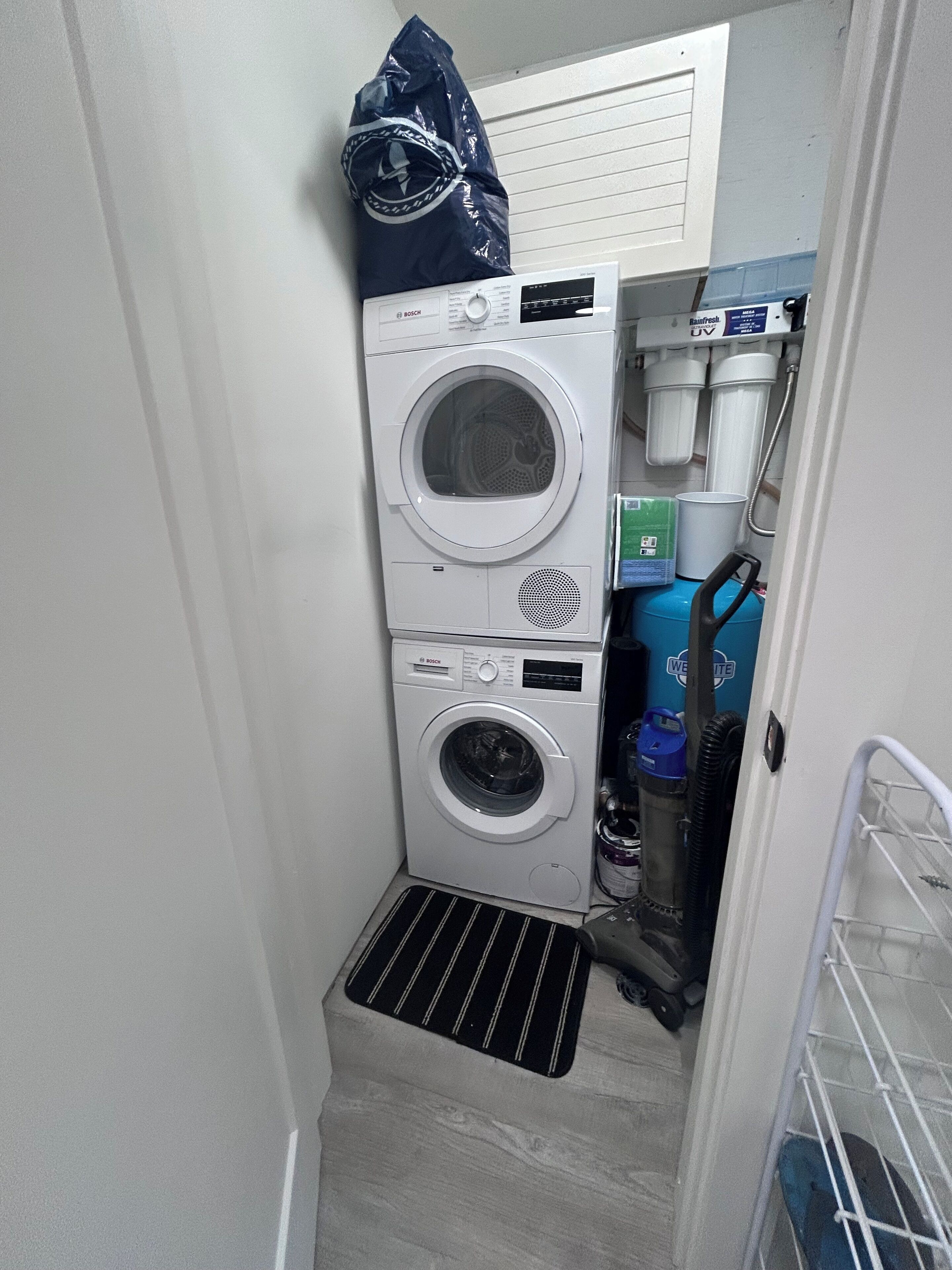 A compact laundry area with two stacked Bosch washing machines, a small sink, and a water filtration system.