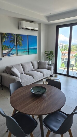 A modern living room with a sofa, a dining table with chairs, a large window with a view, and an air conditioning unit. - Relax, Unwind and Experience Vallarta (Puerto Vallarta)