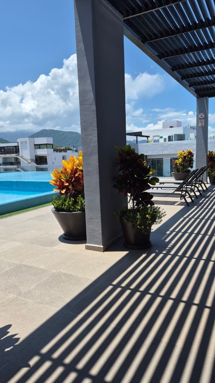A covered outdoor area with a pool, potted plants, and a view of modern buildings in the background.