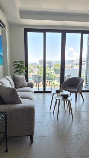 A modern living room with a sofa, armchair, and small table. Large windows offer a view of the cityscape. - Relax, Unwind and Experience Vallarta (Puerto Vallarta)