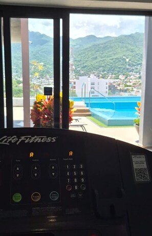 Màquina d'exercici amb panell de control i vista a una piscina i muntanyes al fons.