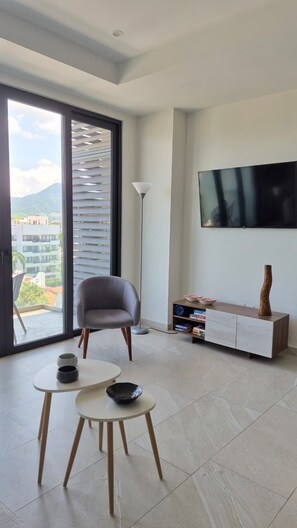 A modern living room with a large TV, a sofa, a dining table with two chairs, and a bookshelf. - Relax, Unwind and Experience Vallarta (Puerto Vallarta)